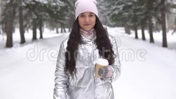 一个心情愉快的女孩手里拿着一杯咖啡走过冬天的森林视频的预览图