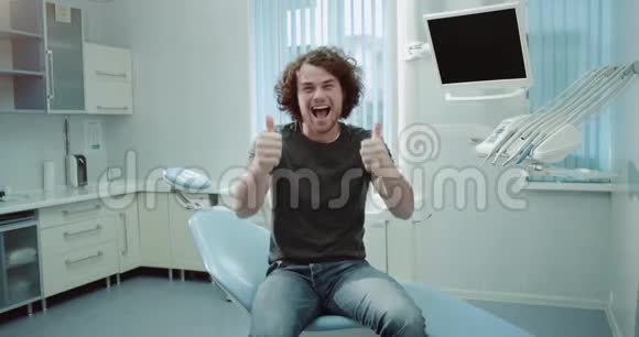 在一家牙科诊所的病人中一个年轻人非常有魅力笑容满面卷发快乐地坐在上面视频的预览图