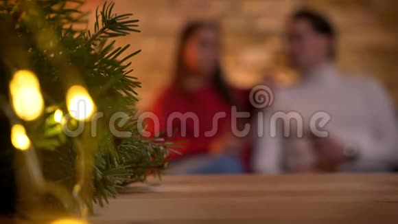 圣诞树上有灯光和模糊的年轻夫妇坐在沙发上在背景上交谈视频的预览图