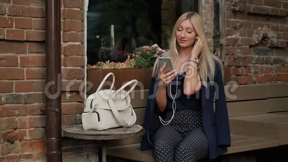 穿西装的年轻商务女性在智能手机上听音乐美丽的金发女郎正躺在长凳上用视频的预览图