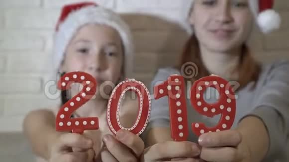 特写蜡烛以数字形式2019在前台戴着圣诞老人帽子的孩子们拿着红色的数字视频的预览图