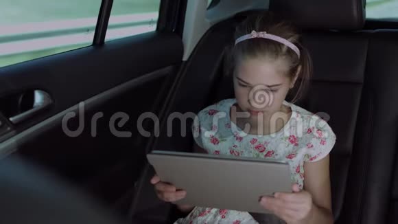 快乐的女孩在车里的平板上看动画片视频的预览图