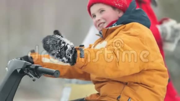 微笑的男孩坐在雪地车上在冬天的森林里呼唤他视频的预览图