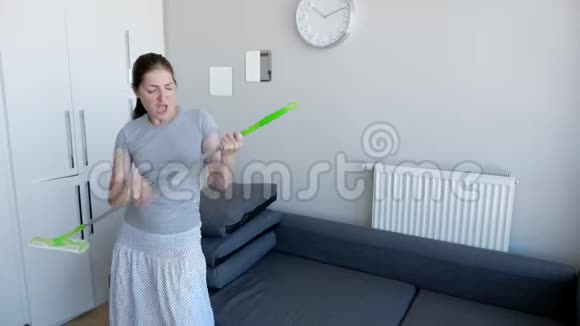 快乐的女人正在用拖把洗地板在她的现代公寓里唱歌跳舞视频的预览图