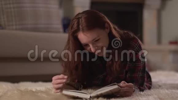 可爱的女人穿着格子衬衫躺在蓬松的地毯上近距离阅读这本书女士翻页微笑放松视频的预览图