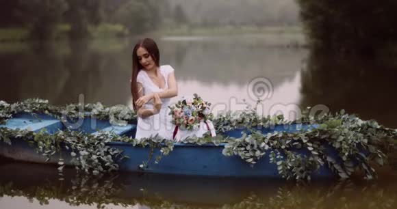 美丽的花束穿着白色连衣裙的年轻女子漂浮在用草药装饰的船上视频的预览图