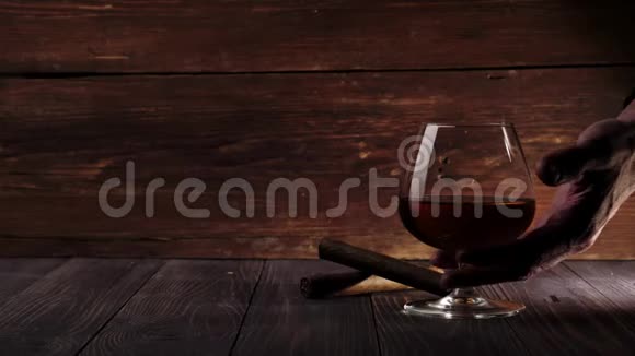 豪华白兰地桌子上有两支雪茄手拿一杯金干邑从木桌上的木制背景视频的预览图