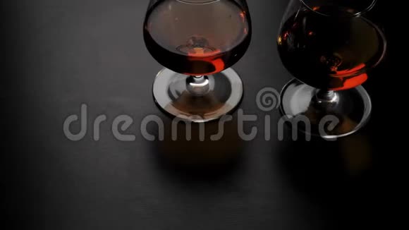 豪华白兰地两杯金色干邑酒在黑桌上旋转玻璃在灯光下眩光白兰地白兰地嗅探器狂欢视频的预览图