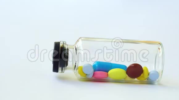 一个带有多色药丸和胶囊的小玻璃瓶滚出框架视频的预览图
