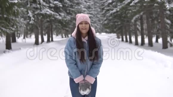 一个心情愉快的女孩站在冬天的森林里微笑着把雪洒在她的头上视频的预览图