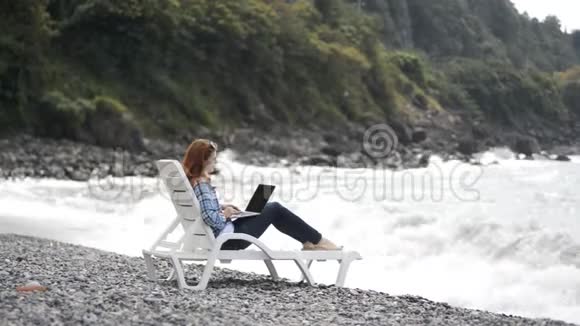 年轻漂亮的女人在海边的现代笔记本电脑上打字视频的预览图