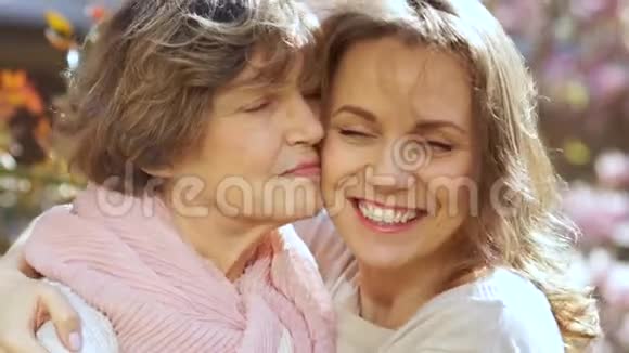母女亲密的春天画像在盛开的花园里女人笑拥抱亲吻视频的预览图