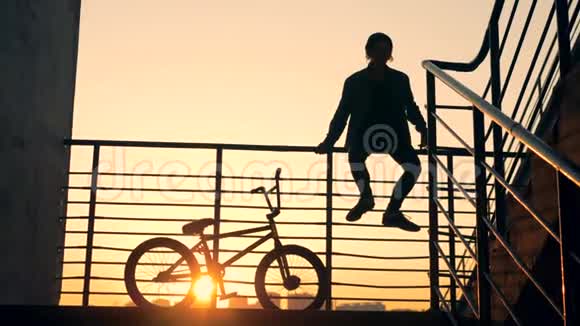 楼梯栏杆上坐着一个男青少年他的自行车在他旁边视频的预览图