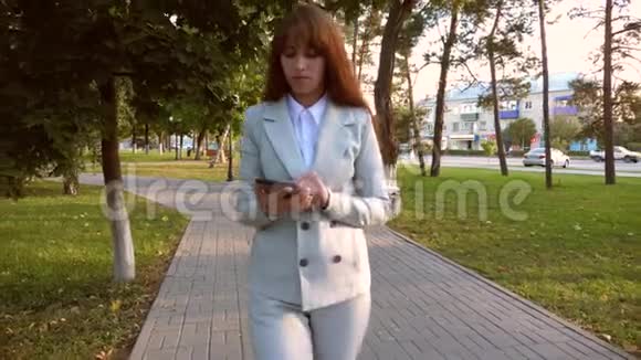商务女性穿着西装手里拿着平板电脑走在傍晚的公园里消磨她的空闲时间制作一个视频的预览图