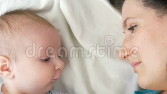 年轻漂亮的黑发妈妈躺在白色的床上和两个月大的新生儿玩耍视频的预览图