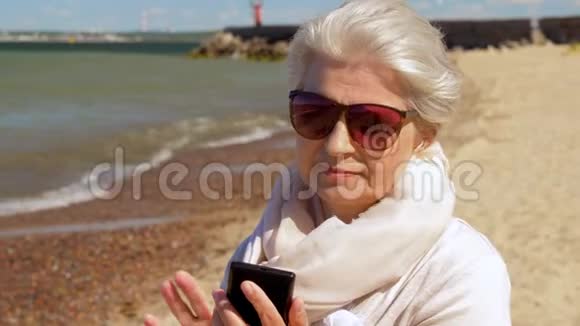 在夏日海滩打电话给智能手机的老妇人视频的预览图