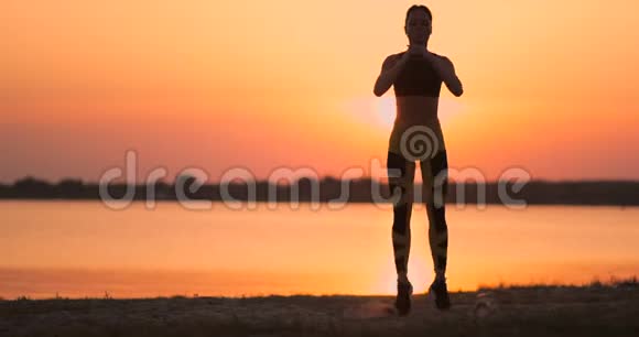 一个女人在日落时在海滩上慢动作地表演静坐锻炼臀部的肌肉视频的预览图