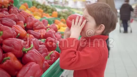 超市里的小男孩闻着红色的保加利亚辣椒商店购物厨房和烹饪用新鲜产品视频的预览图