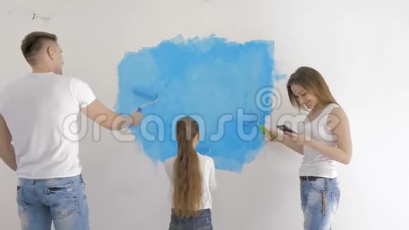 年轻的家庭在母亲查看短信时用滚筒粉刷墙壁视频的预览图