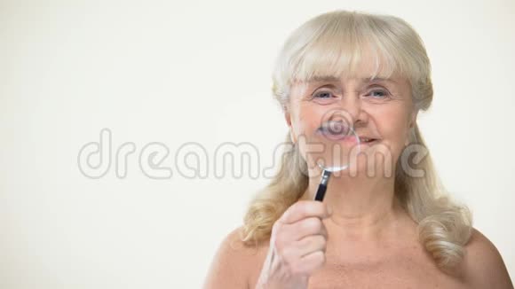微笑老年女士把放大镜放置在皱纹抗衰老化妆品视频的预览图