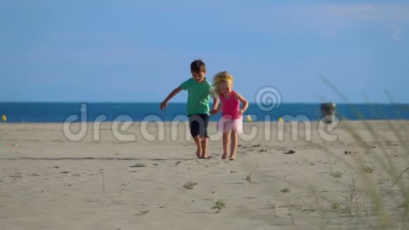 小男孩和小女孩沿着海边的沙滩奔跑视频的预览图