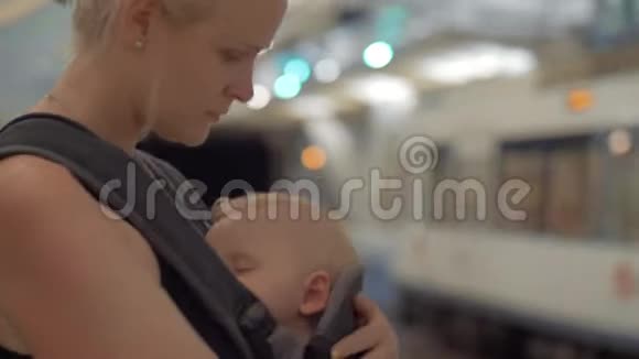 妈妈带着熟睡的孩子在婴儿车里等地铁列车视频的预览图