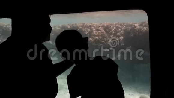 一个未被认出的孩子和他的父母在水下游客的大观察窗口附近的剪影视频的预览图