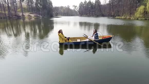 两个年轻漂亮的女孩坐在美丽的倒影湖或河中央的小船上积极的生活方式视频的预览图