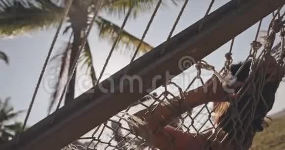 美丽的年轻女子穿比基尼在热带海滩吊床异国情调放松生活方式广告商业视频的预览图
