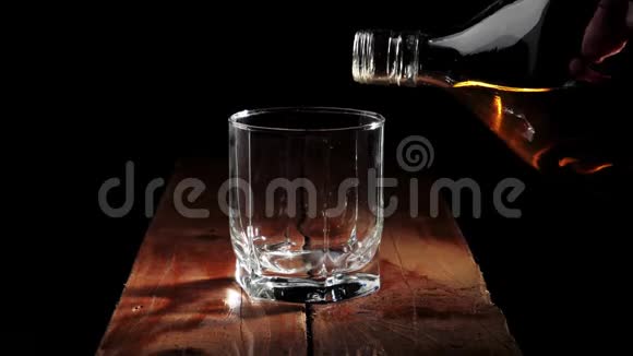 豪华威士忌手把金色的威士忌从一个方形的瓶子倒入一个玻璃在棕色的木制桌子上的黑色背景视频的预览图