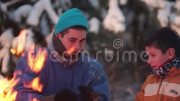冬季森林年轻人和他的弟弟坐在火边聊天视频的预览图