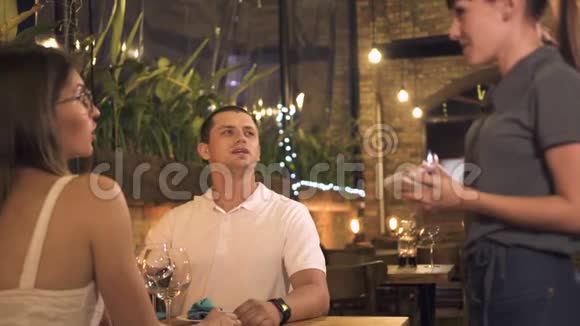 情侣在餐桌上点菜晚上在餐厅吃浪漫晚餐女服务员接受男人和女人的命令视频的预览图