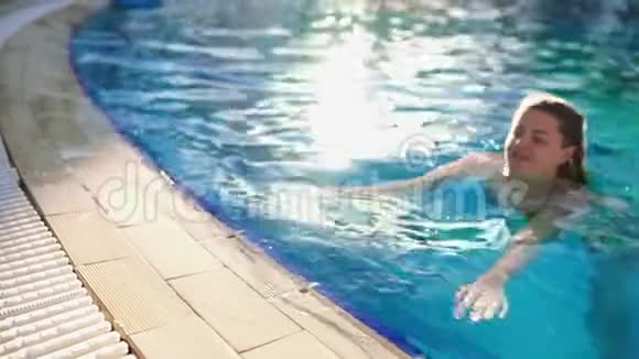在阳光明媚的一天女人在游泳池里用蓝色透明的水游泳放松游泳池水视频的预览图
