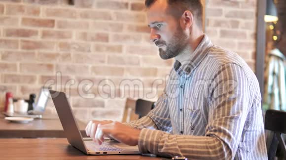 大胡子休闲男在阁楼的笔记本电脑上工作视频的预览图