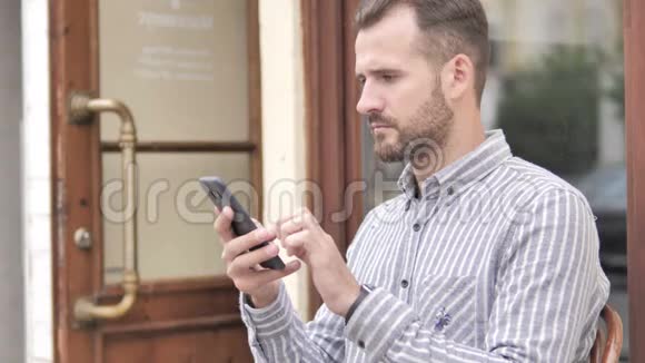男人在户外坐着庆祝智能手机视频的预览图