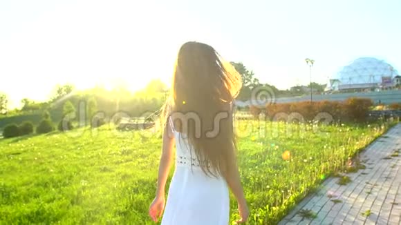 美丽的女孩在公园的绿草上散步在太阳日落的夏日里玩得很开心自由健康幸福年轻快乐视频的预览图