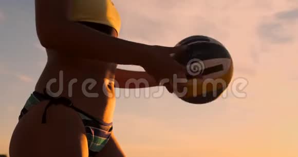 一位身穿比基尼日落时带球的美女正准备在沙滩排球比赛中发球跳跃视频的预览图
