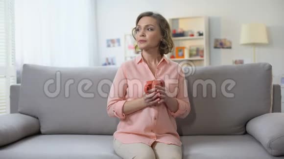坐在家里沙发上喝杯茶的漂亮女人想问题视频的预览图