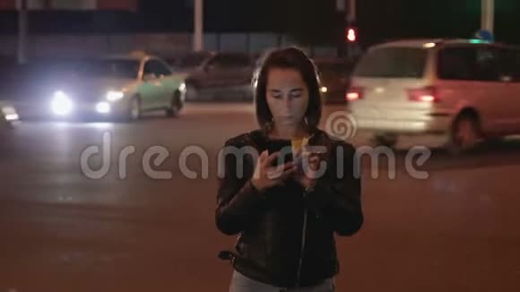 在城市的灯光和汽车的背景下漂亮的女孩晚上拿着电话视频的预览图