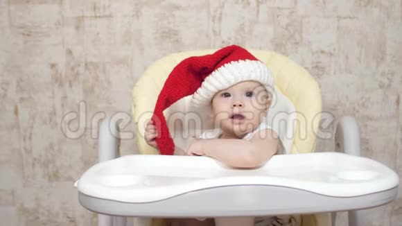 戴着红色圣诞帽的婴儿坐在高椅子上笑着圣诞节新年视频的预览图