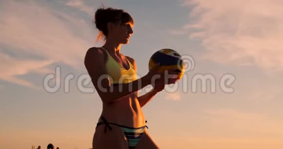 一位身穿比基尼日落时带球的美女正准备在沙滩排球比赛中发球跳跃视频的预览图