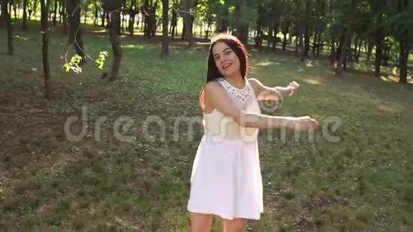 一个快乐的女孩棕色长发穿着白色短裙在公园里玩得很开心视频的预览图