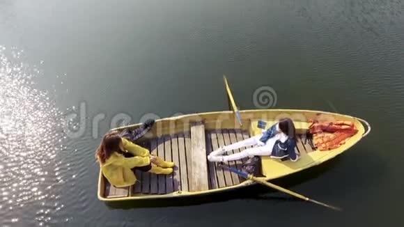 两个年轻漂亮的女孩坐在美丽的倒影湖或河中央的小船上积极的生活方式视频的预览图