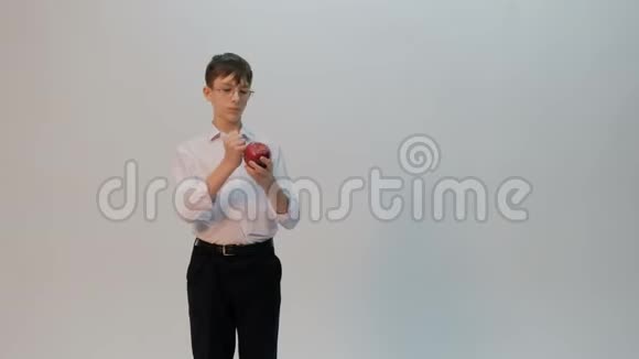 一个学生或一个带着眼镜和一件白色衬衫的小学生把拳头和一个红苹果相比一个长相滑稽的少年表现出不同的视频的预览图
