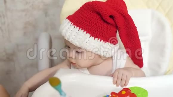 妈妈用坐在儿童座位上的小勺子喂孩子戴着红色圣诞老人帽子圣诞节新年特写视频的预览图