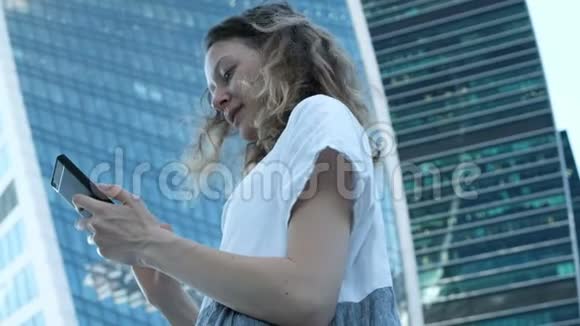 年轻漂亮的女孩在摩天大楼的背景下使用智能手机视频的预览图