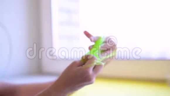 女孩向两边伸展绿色黏液孩子们的手在玩黏液玩具在白色上做黏液时髦的液体玩具棒视频的预览图