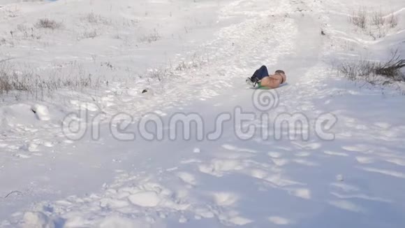女孩在雪橇上翻滚从一个高雪覆盖的滑梯女孩冬天在公园里玩慢动作视频的预览图