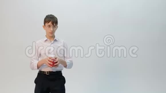 年轻人是学生或小学生戴着眼镜穿着白色衬衫手里拿着一个红苹果十几岁的孩子跳舞时视频的预览图