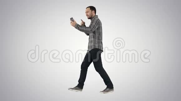 英俊的胡子男人用智能手机录制vlog博客同时在梯度背景下行走视频的预览图